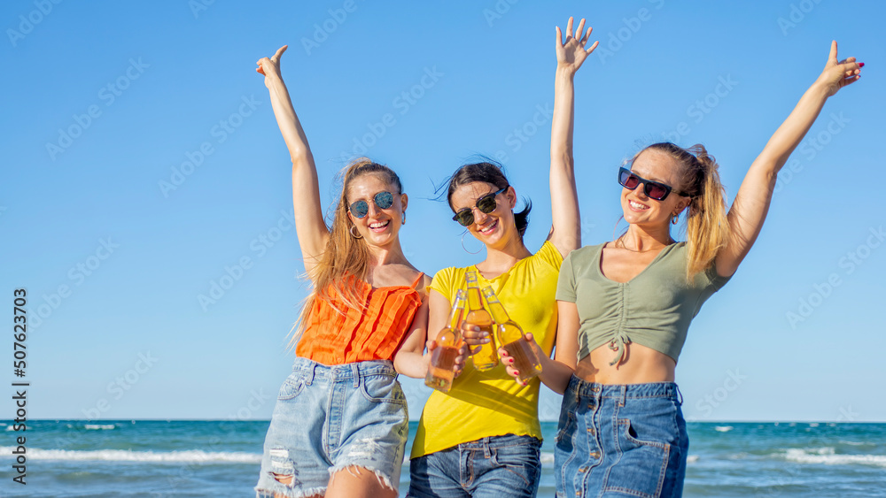 three happy women toasting beers at the beach standing on sand outdoors celebrating summer vacation days on happy hour. friends raising hands on seaside sunset holiday. freedom, genz and party concept three happy women toasting beers at the beach standing on sand outdoors celebrating summer vacation days on happy hour. friends raising hands on seaside sunset holiday. freedom, genz and party concept