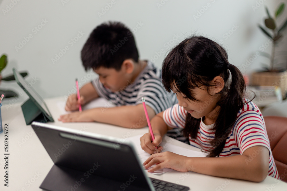 Asian boys and girls enjoy online learning by taking notes and using tablets at home. Asian boys and girls enjoy online learning by taking notes and using tablets at home.