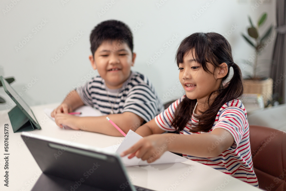 Asian boys and girls enjoy online learning by taking notes and using tablets at home. Asian boys and girls enjoy online learning by taking notes and using tablets at home.
