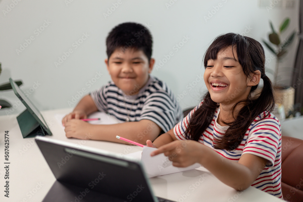 Asian boys and girls enjoy online learning by taking notes and using tablets at home. Asian boys and girls enjoy online learning by taking notes and using tablets at home.