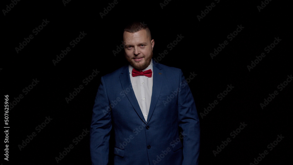 An elegant man in a blue tuxedo and a red tie smiles sweetly against a black background An elegant man in a blue tuxedo and a red tie smiles sweetly against a black background