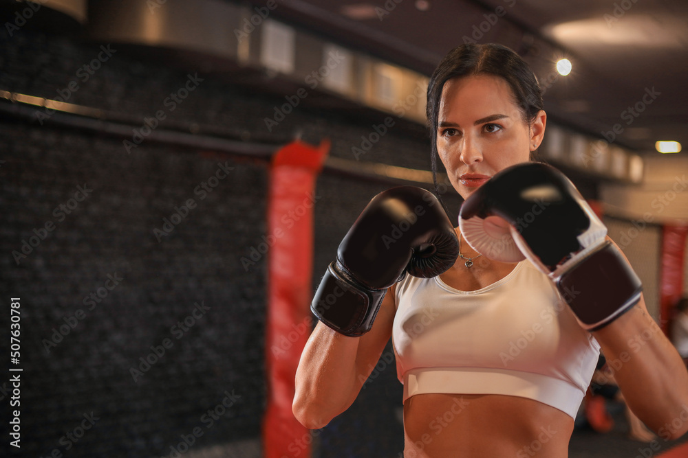 Female in boxing gloves and sportive wear stands in a rack in the boxing hall