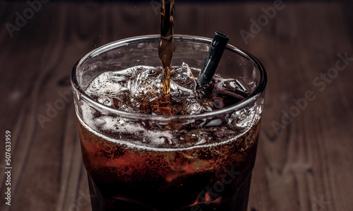Drink. Soda in a glass with ice on a wooden background. The process of pouring soda into a glass with a black straw