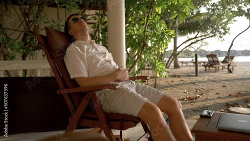 Wallpaper Mural A man rests on a chair on the shores of the Indian Ocean, wearing glasses. The concept of a sleep break while working on a tropical island Torontodigital.ca