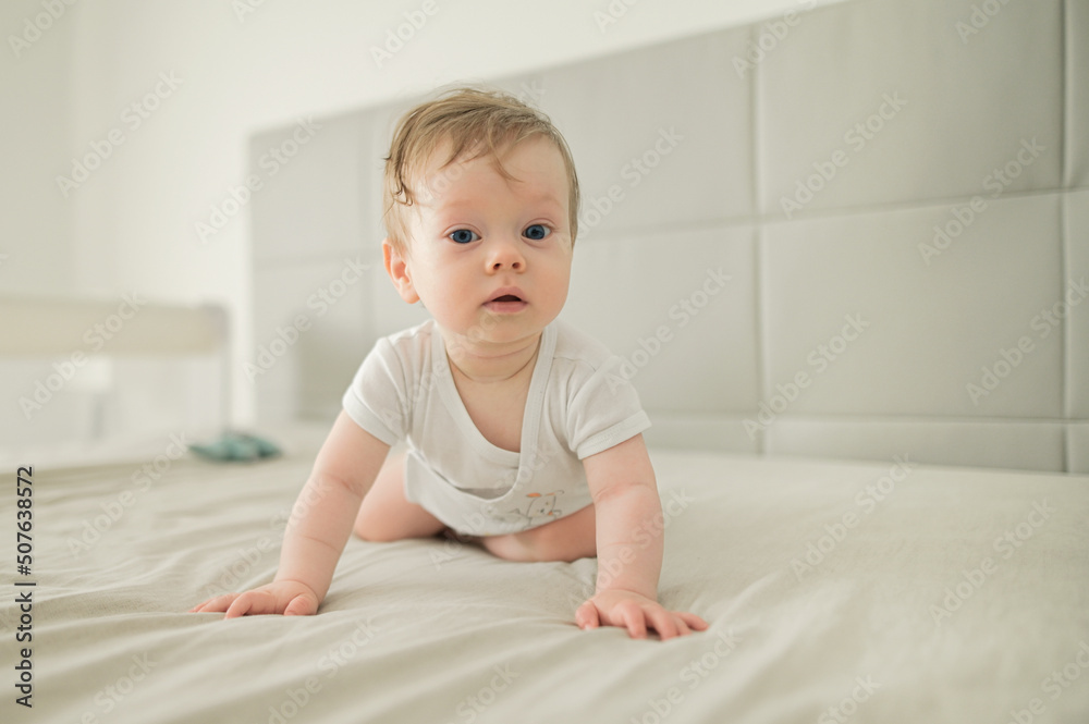 A happy smiling little cute toddler baby boy trying to crawl and playing at home on the bed. Eco friendly toys and motherhood concept.