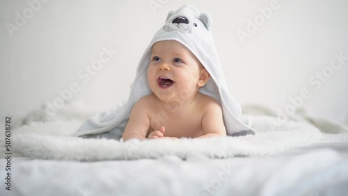 Cute funny little baby boy, relaxing in bed after bath, laughing happily
