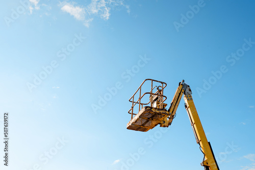 Telescopic boom lift rised up on blue sky background delivered to constraction site ready to be used by steel frame erectors, roofers and painters photo