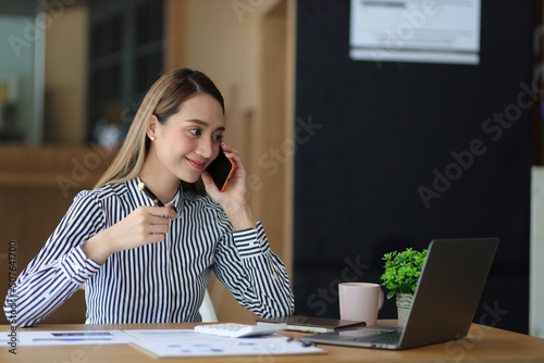 Happy business woman talking on her mobile phone while analyzing her weekly work calendar on her laptop.