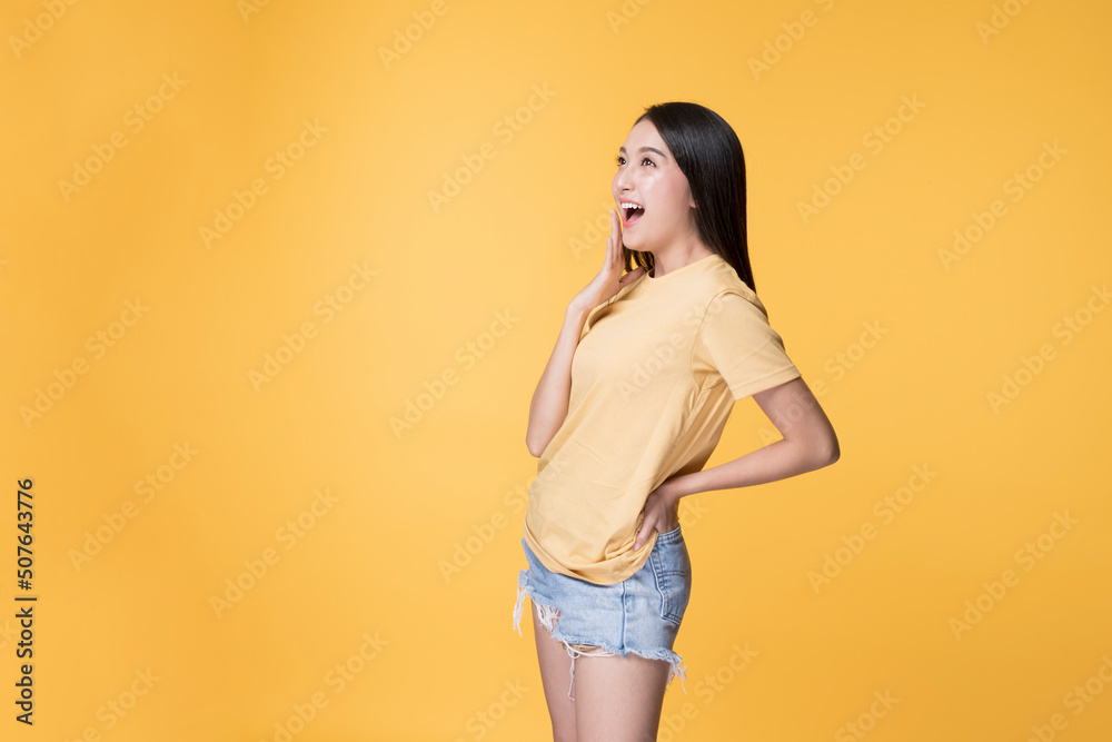 Young Asian Woman making Hand gesture with Surprise Face. Happy Asian Woman wearing Yellow T-shirt standing over yellow background. Portrait of Happy Asian female. Young Asian Woman making Hand gesture with Surprise Face. Happy Asian Woman wearing Yellow T-shirt standing over yellow background. Portrait of Happy Asian female.