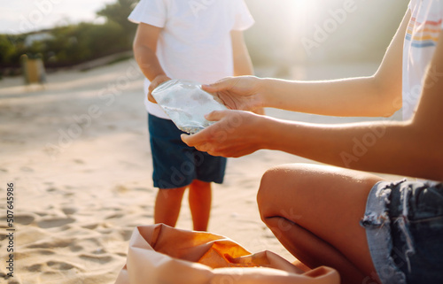 Scavengery. Child with mother collects plastic, garbage on the beach by the sea. Empty used dirty plastic bottles. Environmental pollution on the Sea coast. photo