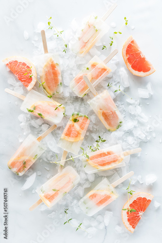 Refreshing grapefruit thyme popsicles scattered around on a bed of ice.