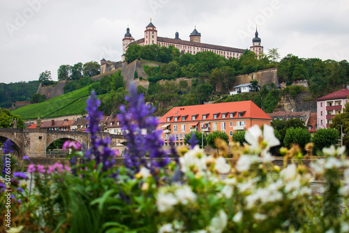 Marienberg Fortress upon a vineyard hill above the Old Bridge and Main river seen from the other site of the river through colorful blooming summer or spring flowers
