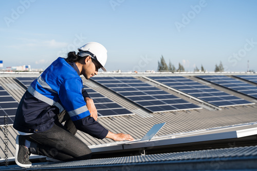 Asian technician installing inspection or repair solar cell panels on background field of photovoltaic solar panels solar cells on roof top factory.