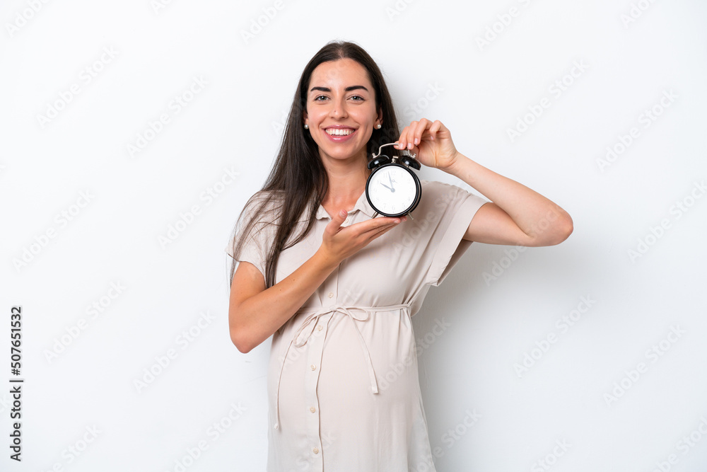 Fototapeta premium Young caucasian woman isolated on white background pregnant and holding clock