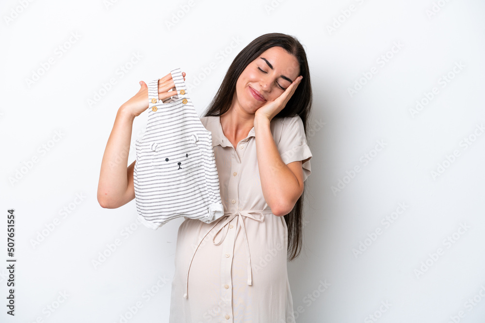Young caucasian woman isolated on white background pregnant and holding baby clothes