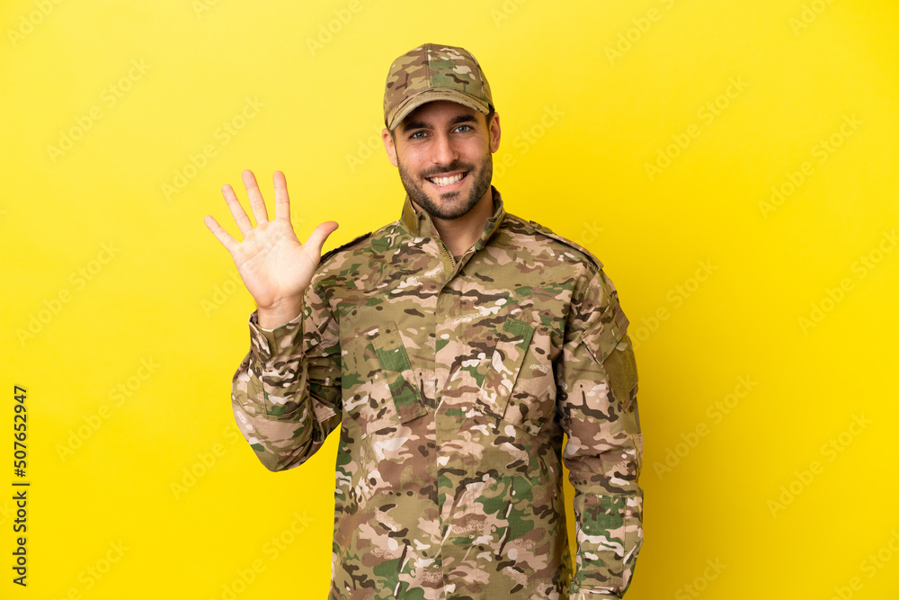 Military man isolated on yellow background counting five with fingers Military man isolated on yellow background counting five with fingers