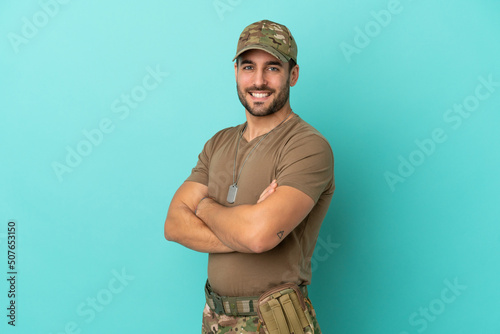 Military with dog tag over isolated on blue background with arms crossed and looking forward
