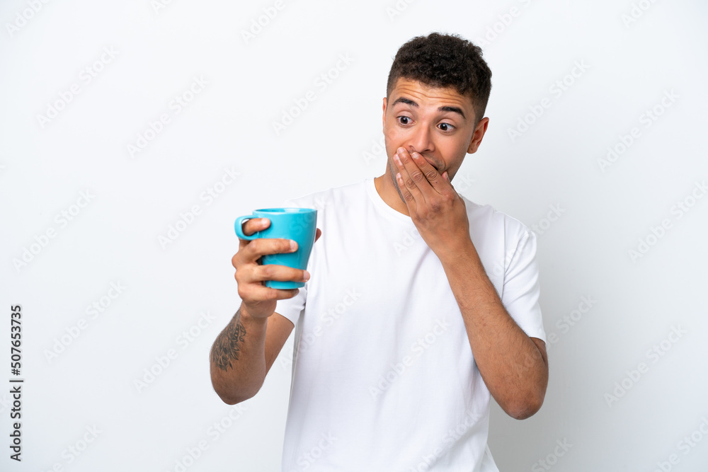 Young Brazilian man holding cup of coffee isolated on white background with surprise and shocked facial expression Young Brazilian man holding cup of coffee isolated on white background with surprise and shocked facial expression