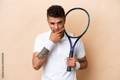Young brazilian handsome man playing tennis isolated on beige background thinking © luismolinero