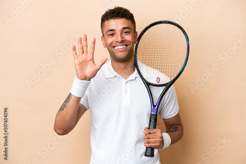 Young brazilian handsome man playing tennis isolated on beige background counting five with fingers