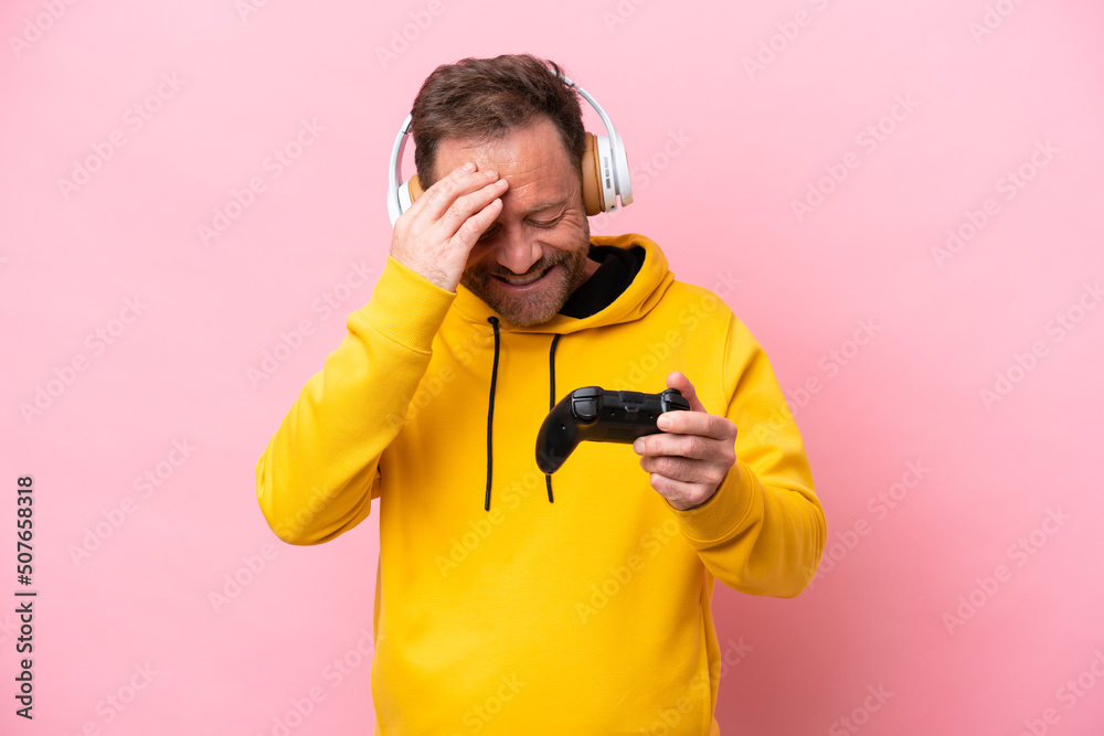 Middle age man playing with a video game controller isolated on pink background laughing Middle age man playing with a video game controller isolated on pink background laughing