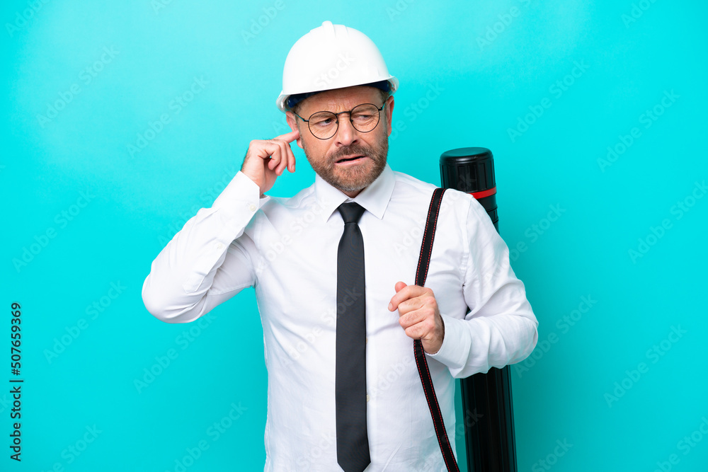 Middle age architect man with helmet and holding blueprints isolated on blue background frustrated and covering ears Middle age architect man with helmet and holding blueprints isolated on blue background frustrated and covering ears