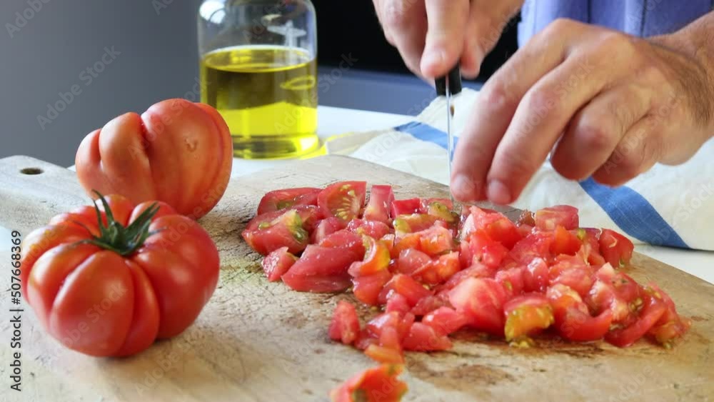 Man's hands dicing fresh tomatoes on a wooden board in a kitchen. Man's hands dicing fresh tomatoes on a wooden board in a kitchen.