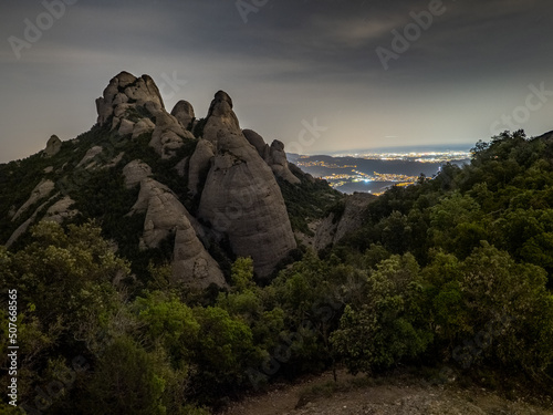 Paisaje de la montaña del parque natural de Montserrat por la noche con las luces de fondo de Barcelona (Cataluña, España).