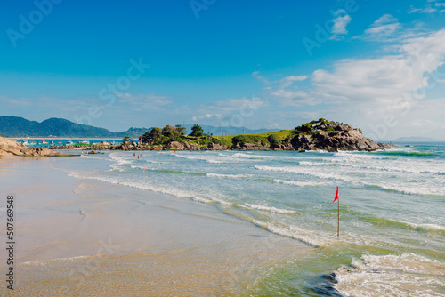 Matadeiro beach with rocky island and ocean with waves on sunny day. Holiday beach in Brazil, Florianopolis