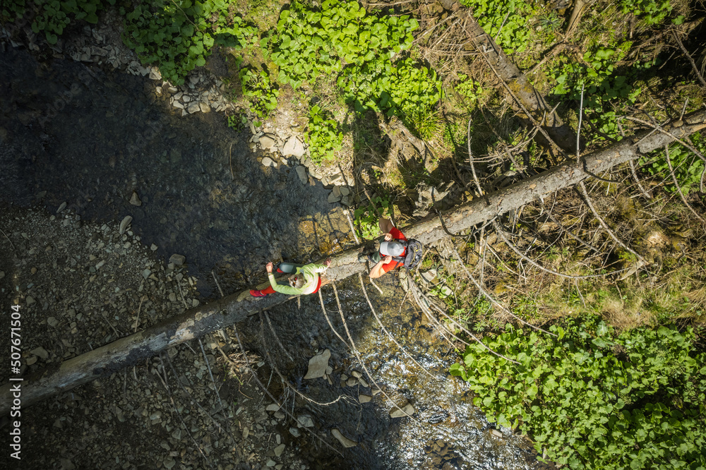 Naklejka premium Hiking Couple Crossing River Walking Along Fallen Tree Aerial View.