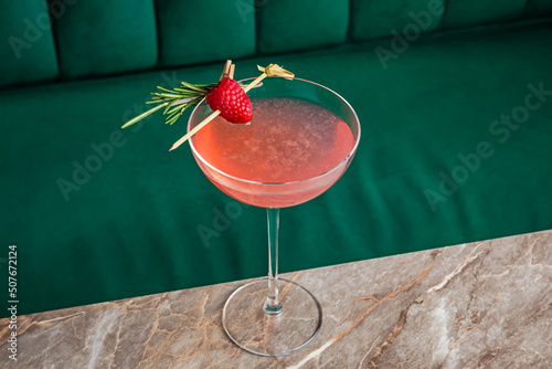 A pink sour alcoholic cocktail with raspberry and rosemary served in a coupe glass photo