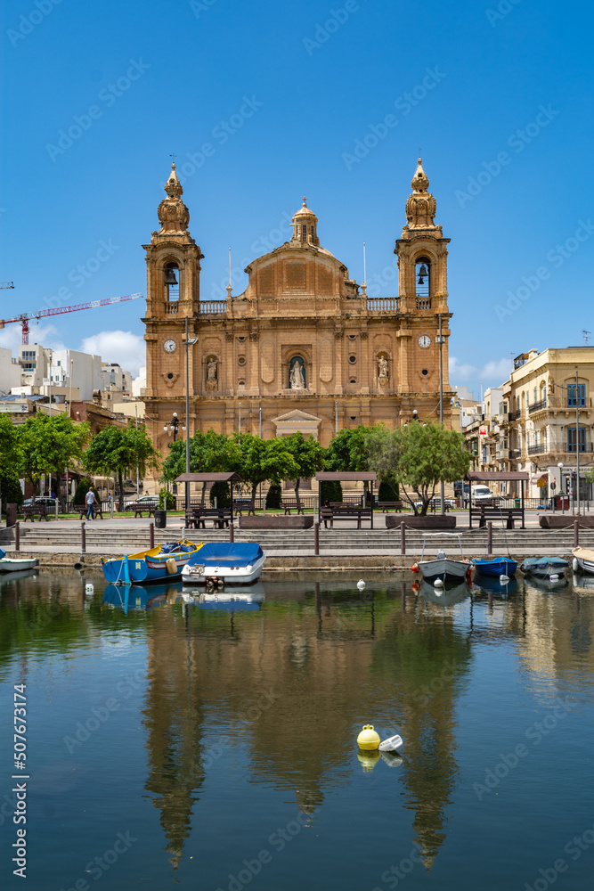 The Parish church of Saint Joseph being reflected on the surface of the sea water in the creek in Msida, Malta