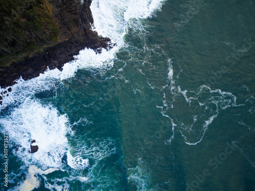 View from above. Beautiful seascape. Dark turquoise with white foamy waves ocean water, hilly. uneven shore covered with green moss. Beauty of nature, environmental protection.