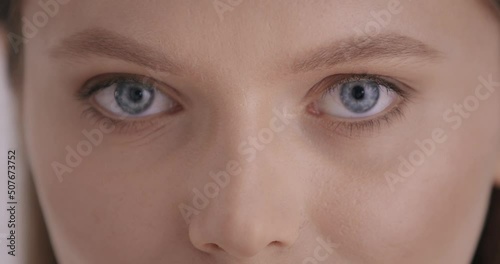 Beauty. Close up portrait of stunning young lady with natural blue eyes posing in studio. Caucasian fashion model with nude makeup and hairstyle over grey background.