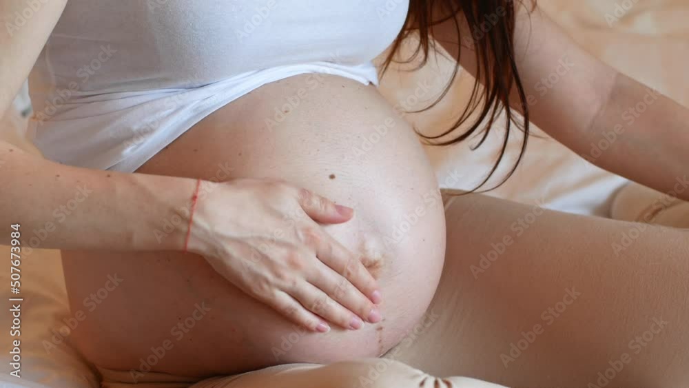 Close-up of a pregnant woman caressing her large belly.

