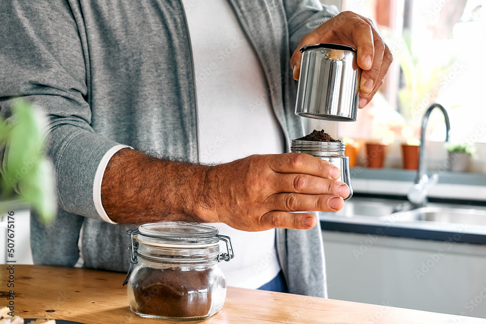 Man preparing classic Italian coffee in the mocha in the kitchen. Pouring coffee from moka pot into small glass coffee cup. Coffee brake. Morning habit.