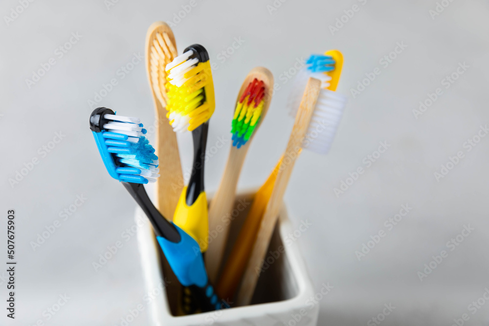 Close-up of a set of multicolored toothbrushes in a glass on a gray background.Dentistry concept.Oral care. The concept of cosmetic products for the bathroom.Side view, copy space.Dental hygiene Close-up of a set of multicolored toothbrushes in a glass on a gray background.Dentistry concept.Oral care. The concept of cosmetic products for the bathroom.Side view, copy space.Dental hygiene