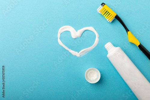 Symbol of heart and love from toothpaste. A tube of toothpaste and a toothbrush on a blue background. Refreshing and whitening toothpaste. Copy space for text. Flat lay