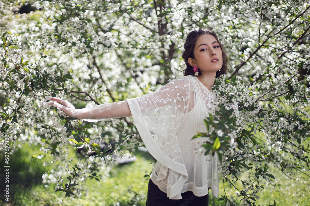portrait of a young beautiful woman in white clothes standing next to a blooming cherry tree in spring. portrait of a young beautiful woman in white clothes standing next to a blooming cherry tree in spring.