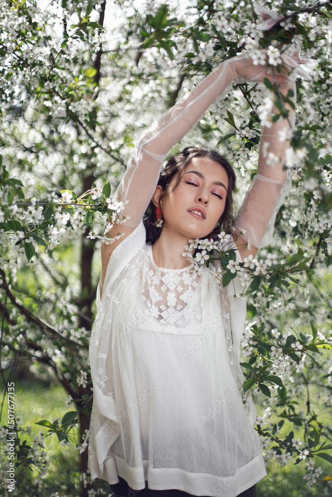 portrait of a young beautiful woman in white clothes standing next to a blooming cherry tree in spring. portrait of a young beautiful woman in white clothes standing next to a blooming cherry tree in spring.