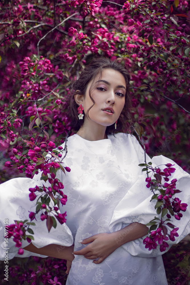 portrait sexy young woman in a white dress and purple tights stands by the blooming purple cherry trees in spring. portrait sexy young woman in a white dress and purple tights stands by the blooming purple cherry trees in spring.
