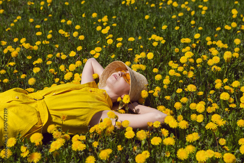 woman in a yellow dress, hat and yellow glasses lies on a field of dandelions in summer.