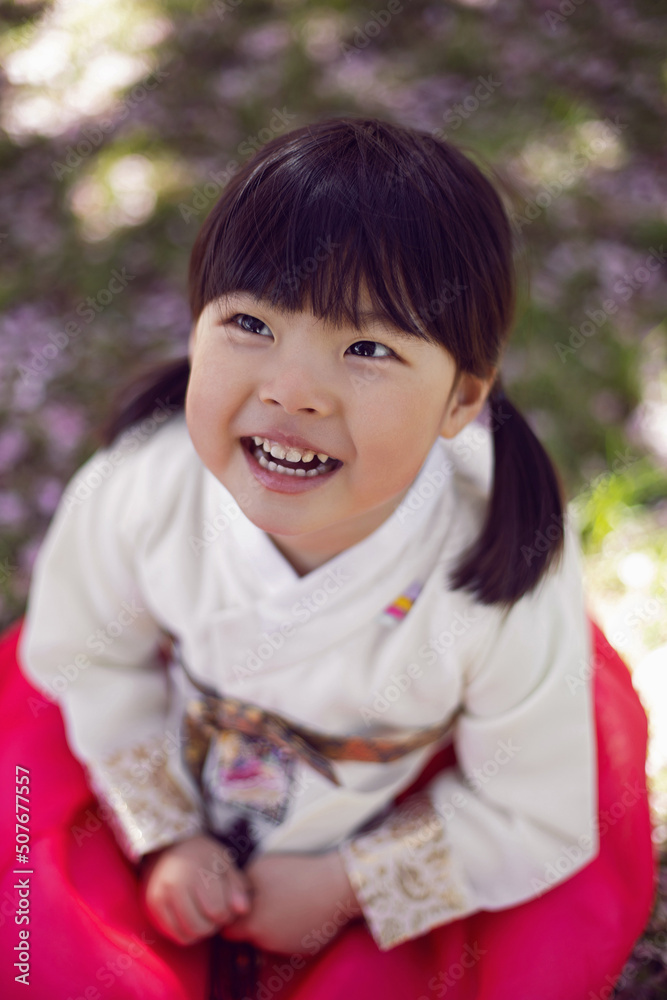 Korean girl child in a national costume walks in a garden with cherry blossoms in spring. Korean girl child in a national costume walks in a garden with cherry blossoms in spring.