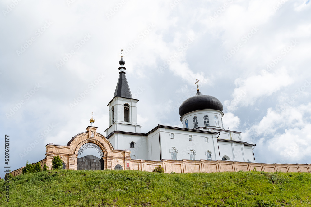 The white church stands on the mountain against the background of an overcast sky, clouds float, a golden cross is fixed on the dome of the temple, a Christian shrine.