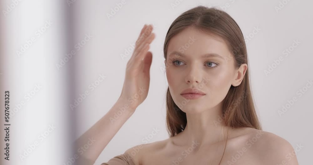 Hair beauty. Tender young woman adjusting her long natural hair while standing in studio. Beautiful female model with healthy clear skin on face posing over grey background. Hair beauty. Tender young woman adjusting her long natural hair while standing in studio. Beautiful female model with healthy clear skin on face posing over grey background.