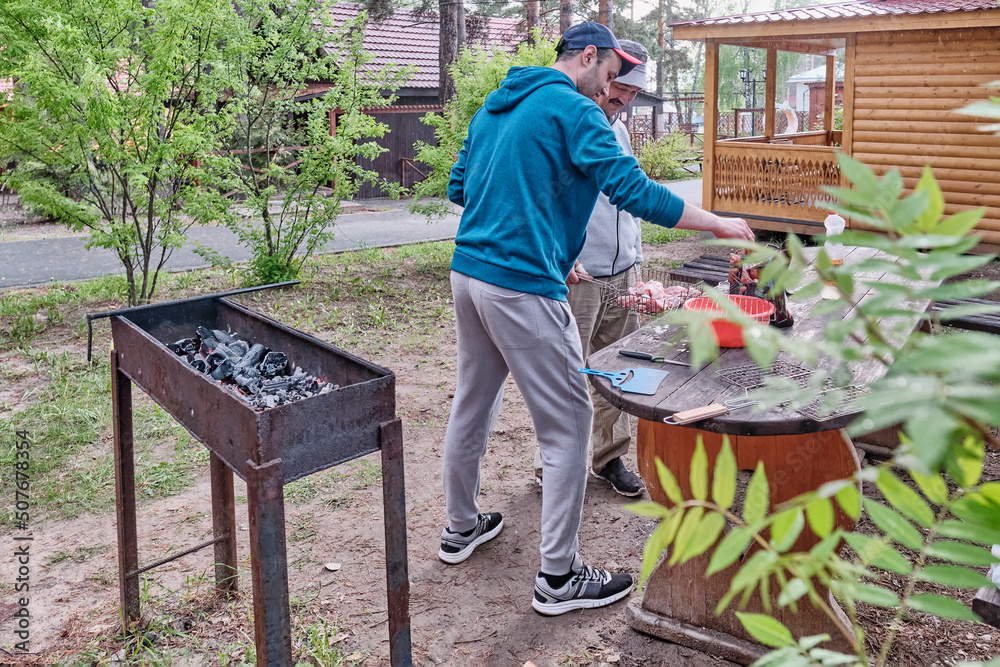 Asian senior man and his adult son placing pieces of raw meat on grill for barbecues in backyard. Asian senior man and his adult son placing pieces of raw meat on grill for barbecues in backyard.