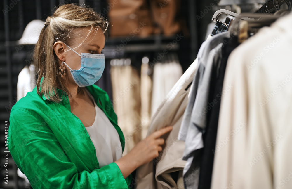 Woman in medical mask choosing clothes in outlet store.