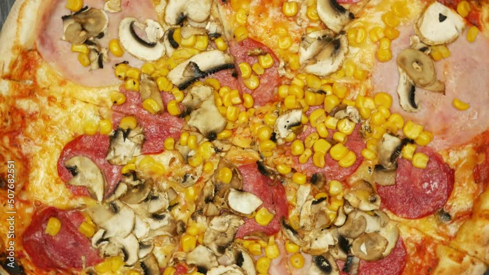 Top view of fresh baked pizza with salami, corn, mushrooms rotating close up. Pizzeria and fast food concept Top view of fresh baked pizza with salami, corn, mushrooms rotating close up. Pizzeria and fast food concept