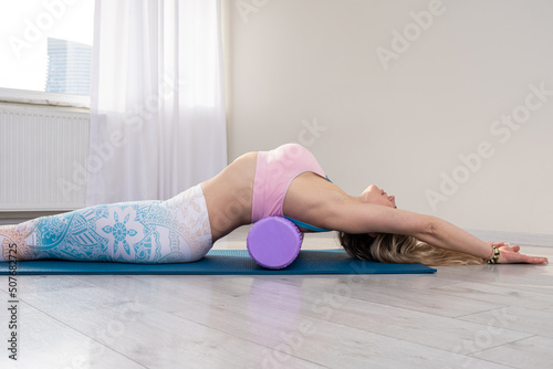 Fit women massaging and stretching muscles with foam roll on yoga mat 