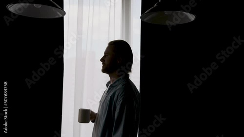 silhouette of a man drinking coffee near the window at home
